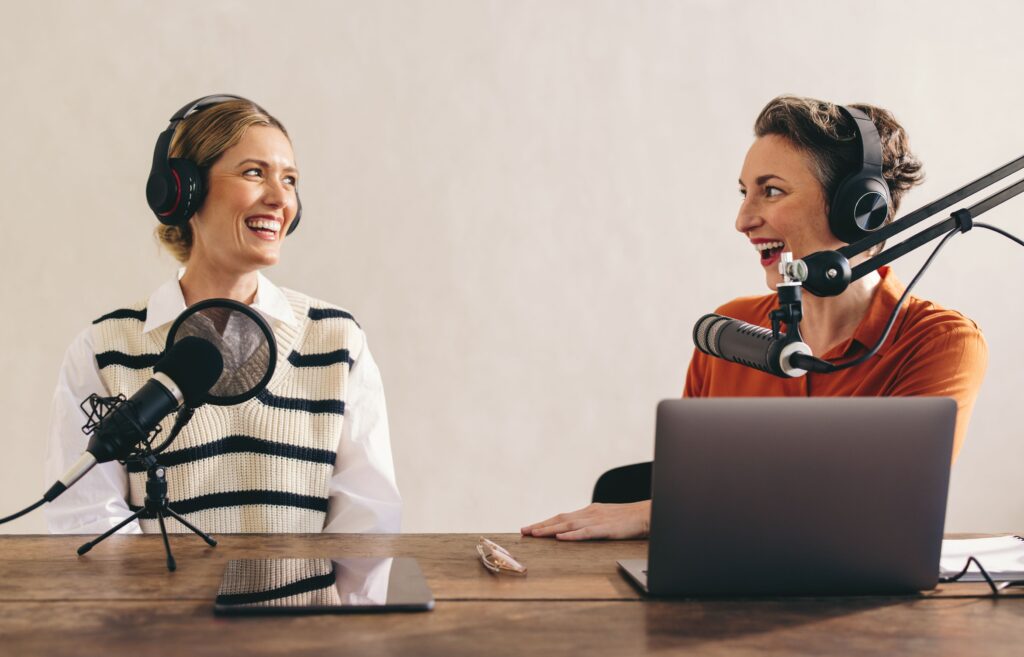 dos mujeres haciendo un podcast en español en una oficina, que tiene dos micrófonos y una laptop